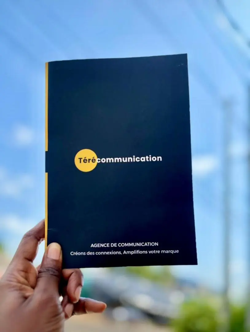 La brochure de Téré Communication tenue à la main, en extérieur